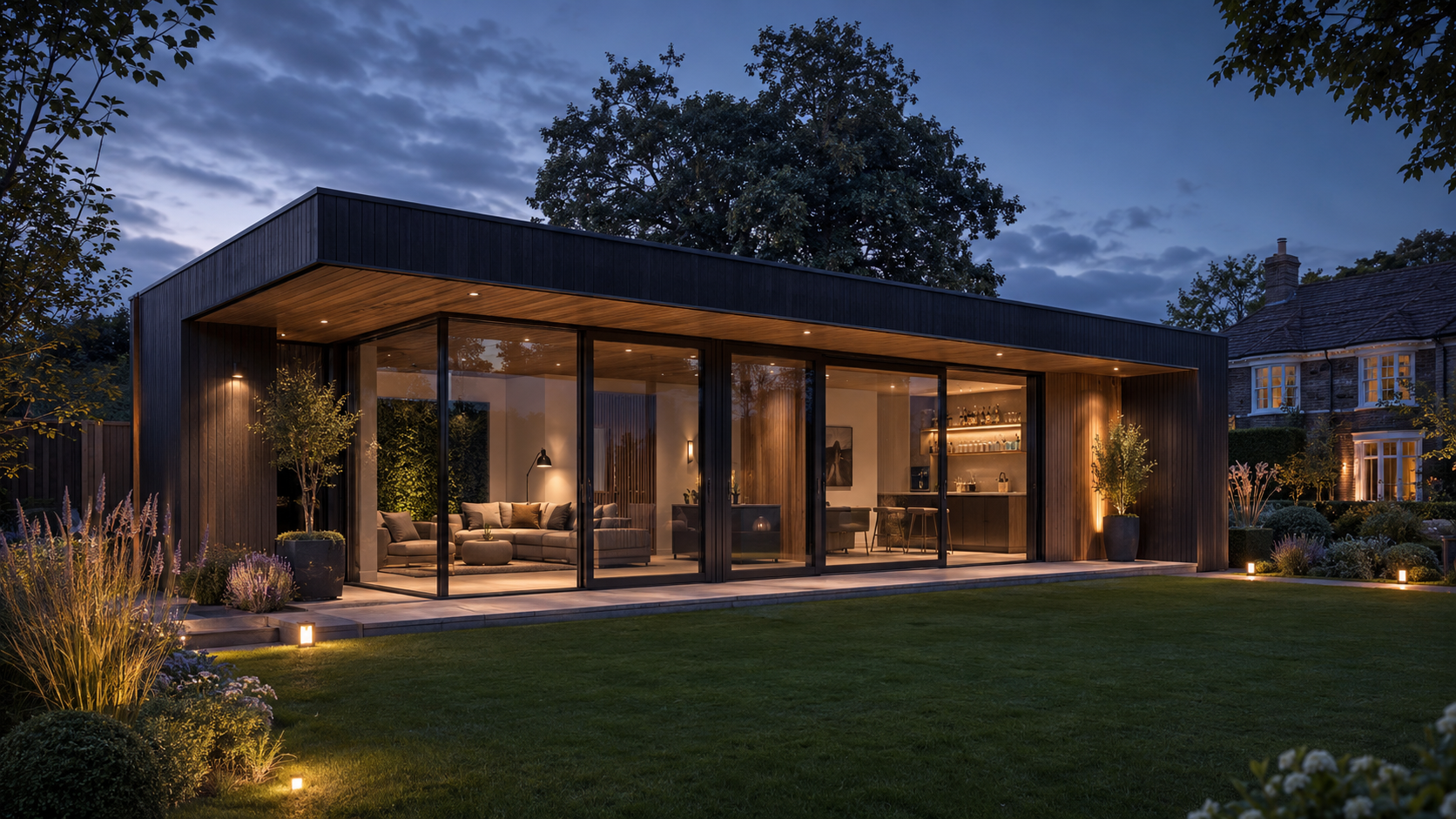 Luxury black-clad garden building with full-height glazing and warm interior lighting at dusk